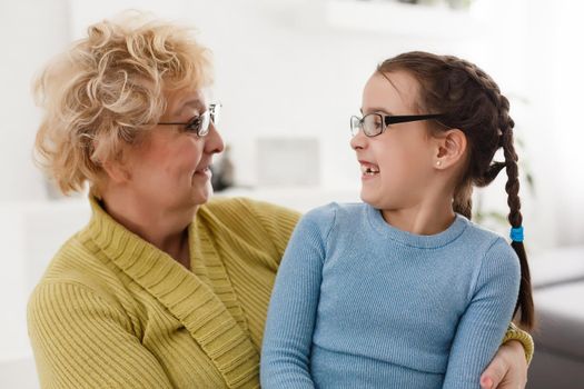 Senior woman hugging granddaughter while sitting on sofa at home