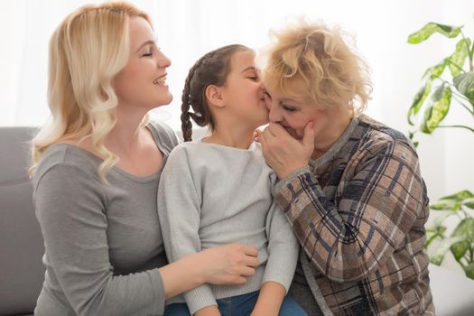Three generations of women. Beautiful woman and teenage girl are kissing their granny while sitting on couch at home