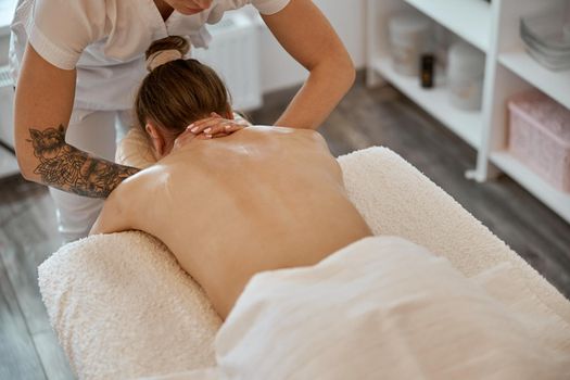 Professional confident massage master is doing procedures to caucasian woman in minimalistic modern cabinet