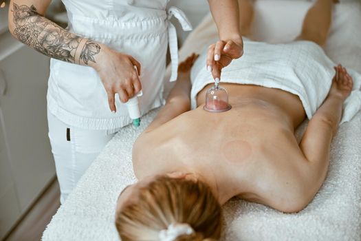 professional female specialist is doing cupping therapy on the back of beautiful caucasian lady