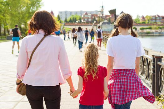 Outdoors portrait of mother and two daughters. Holding hands walking down the street, back view.