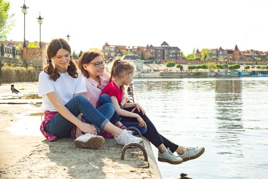 Outdoors portrait of mother and two daughters. Watching the water. Background nature, park, river.