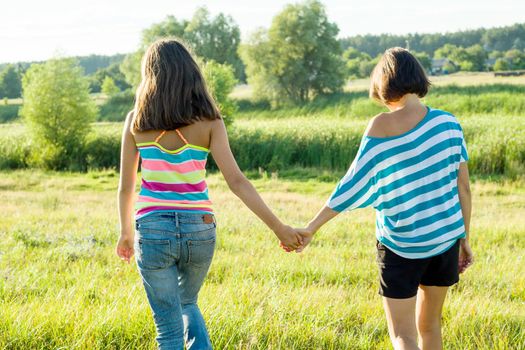 Mother and teen daughter holding hands, back view. Photo on nature in a sunny summer day