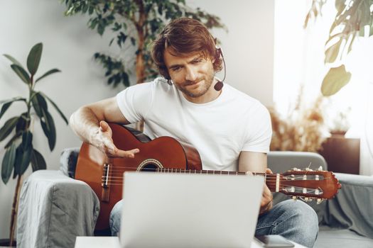 Young man watching guitar tutorial on his laptop at home