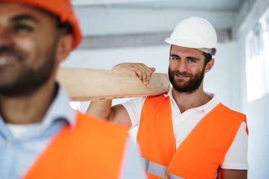 Two young men builders carrying wood planks on construction site, close up photo