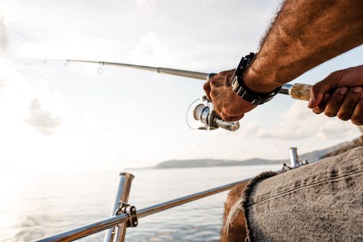 Close up photo of male hands holding fishing rod while fishing on sailboat in open sea