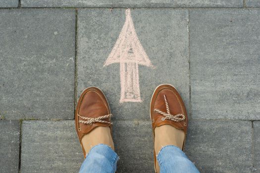 Female feet with arrow painted on the asphalt