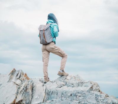 Unrecognizable explorer young woman with backpack standing on peak of cliff and looking into the distance