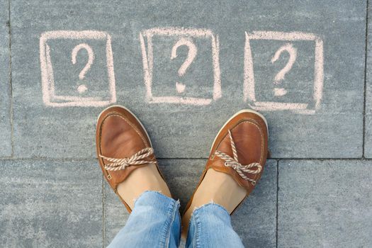 Woman feet with 3 question marks in front of her legs painted on the grey sidewalk