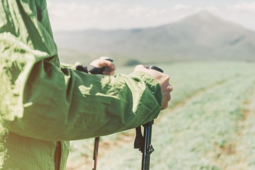 Hiker man holding trekking poles on background of summer mountains, close-up image of hands.