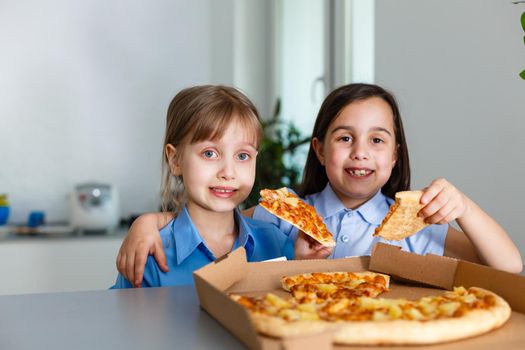 Two happy little child girl friends eating pizza slices.