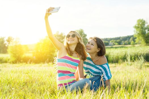 Portrait of beautiful adult mother and her daughter teenage girl making a selfie using a smart phone and smiling.