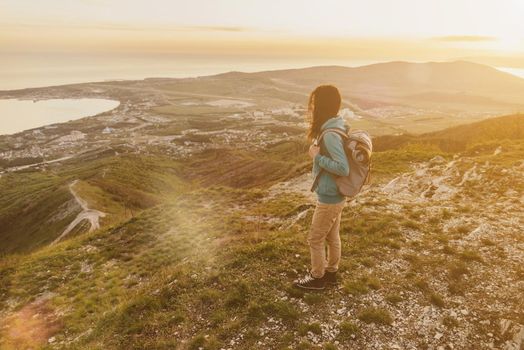 Traveler young woman with backpack standing on peak of mountain at sunset. Image with sunlight effect