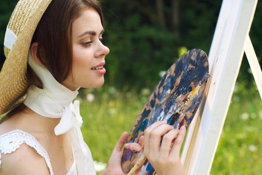 woman with a palette of paints painting a picture outdoors close-up. High quality photo