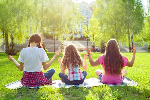 Three young girls doing yoga pose outdoor, yoga at sunset in the park, back view