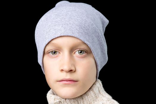Close up portrait of cute teenage boy. Handsome stylish boy in hat and knitted jumper looking at camera. Preteen child posing in studio against black background