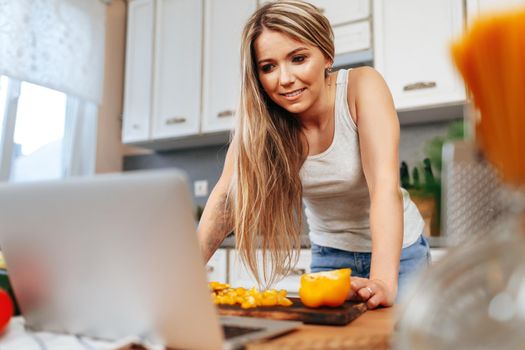Young pretty woman cooking something in her kitchen with laptop