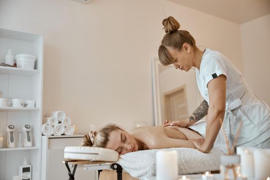 Professional confident massage master is doing procedures to caucasian woman in minimalistic modern cabinet