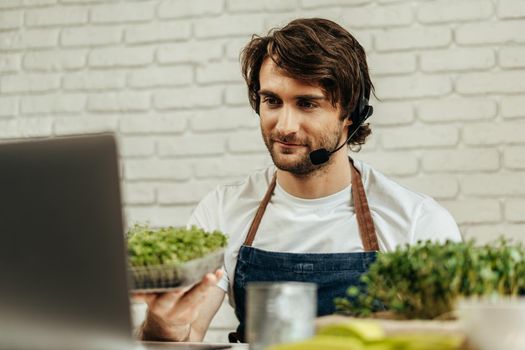 Handsome bearded man sells plant sprouts and seedlings online using laptop by video call