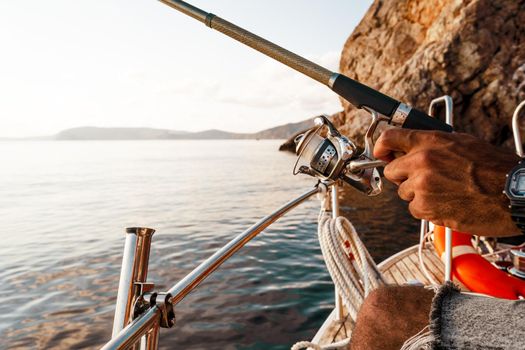 Close up photo of male hands holding fishing rod while fishing on sailboat in open sea