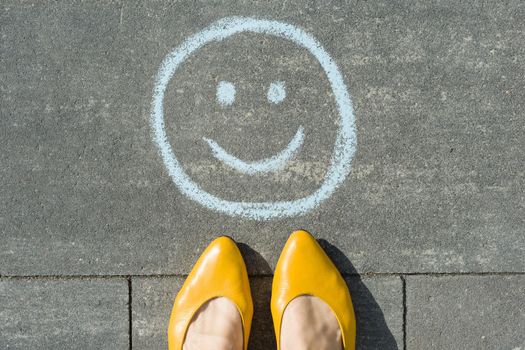 Symbol of happy smiley drawn on the asphalt and woman feet.