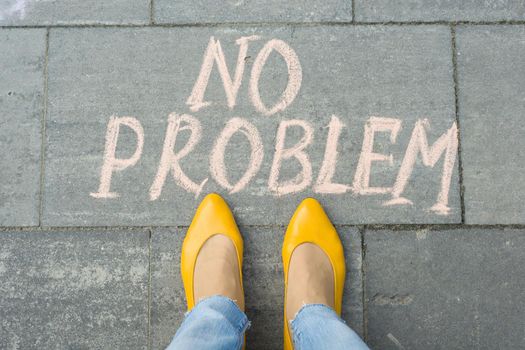 Female feet with text no problem written on grey sidewalk.