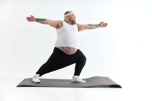 Sporty fat man with beard and tattoos is doing yoga