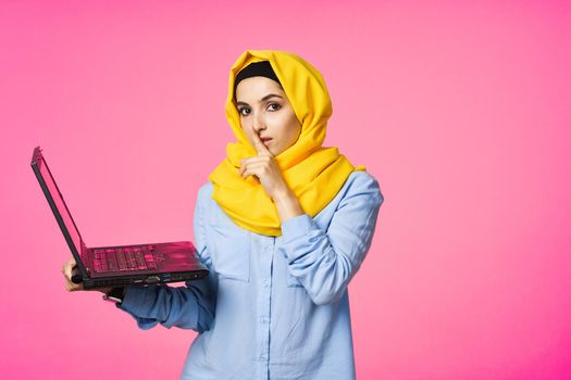 muslim woman in yellow hijab with laptop technology student pink background. High quality photo