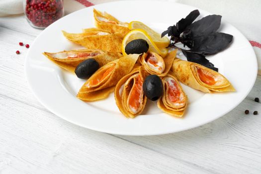 Russian pancakes stuffed with salted salmon on white wooden table background