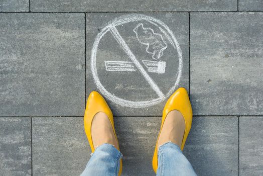 Female feet with picture no smoking painted on the grey sidewalk.