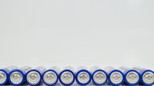 Lots of AA alkaline batteries on a white glossy background with reflection with copy space lined up in one line. Ukraine, Kiev - January 7, 2021