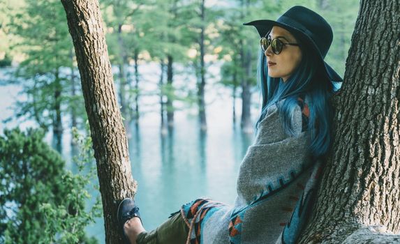 Fashionable young woman resting on tree in spring park near the lake.