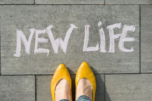 Female feet with text new life written on asphalt.