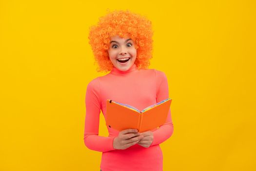 Happy girl child with orange hair in pink poloneck smile holding school book yellow background, education.