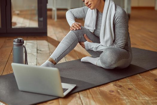 Cropped head of relaxed sporty female sitting on mat with bottle of water in front of notebook