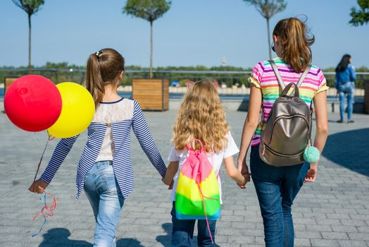 Back view of children schoolgirls holding hands walk together on urban road outdoors background.