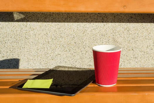 Street bench, tablet with pasted sticker, a cup of coffee