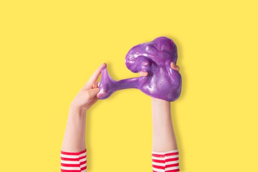 Teenager girl hands and purple shiny slime. Child girl plays with slime isolated on yellow. Home educational games or DIY concept. Top view, flat lay banner.