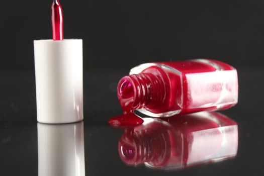 Burgundy red lacquer for leggings flows from the bottle of the bottle close-up view from the side on a black background with a copyspace.