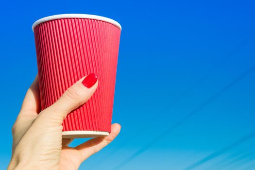 Red paper glass in a female hand, background blue clear sky