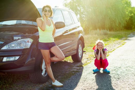 A woman is standing near a broken car. A car on a country road, a woman calls asking for help