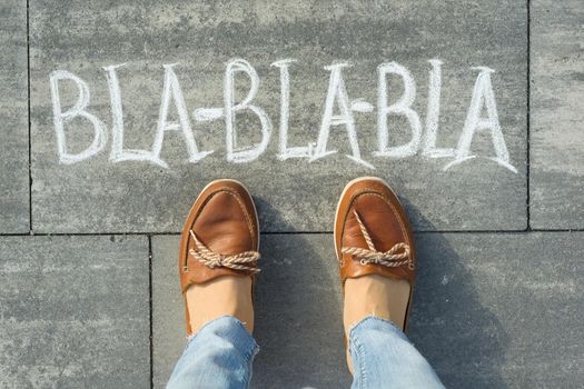 Female feet with text bla-bla-bla written on grey sidewalk.