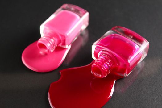 Beauty background two bottles of nail polish bottles red or burgundy pink spill poured on the table on a black background with a copyspace .