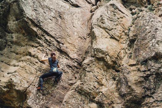 Sporty young woman free climbing on rock outdoor.