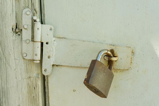 Rusty closed lock on old wooden white cracked painted door.