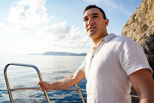 Young man in white shirt standing on the nose yacht in the open sea