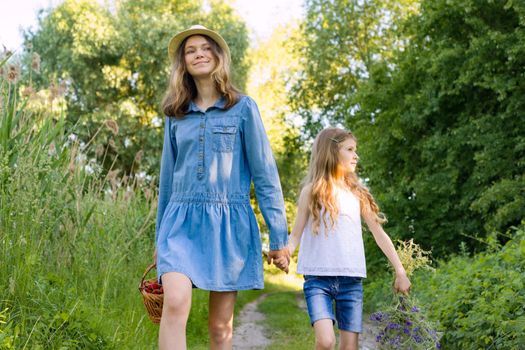 Children girls on forest road holding hands. Sunny summer day, girl holding basket with berries.