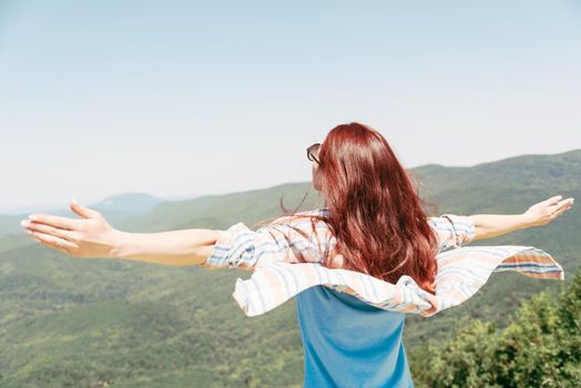 Freedom happy young woman standing with raised arm in windy weather high in the summer mountains.