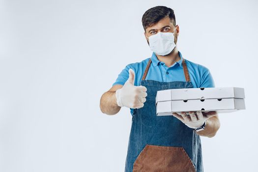 Pizza delivery man in medical gloves and mask against grey background. Safe service while coronavirus covid-19 outbreak