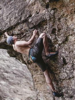 Sporty shirtless young man free climbing on rock outdoor.